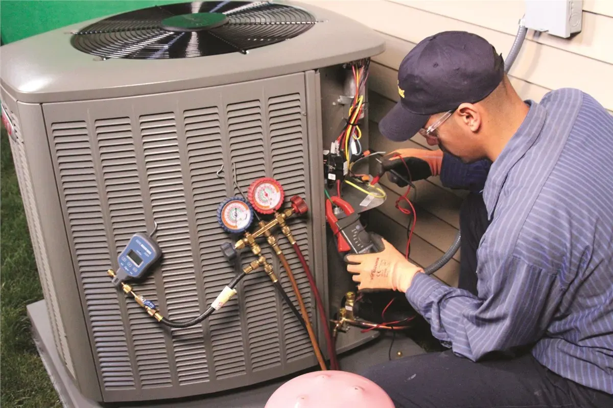 A close view over a technician shoulder as he probes the contactor inside an open condenser cabinet with a clamp meter.